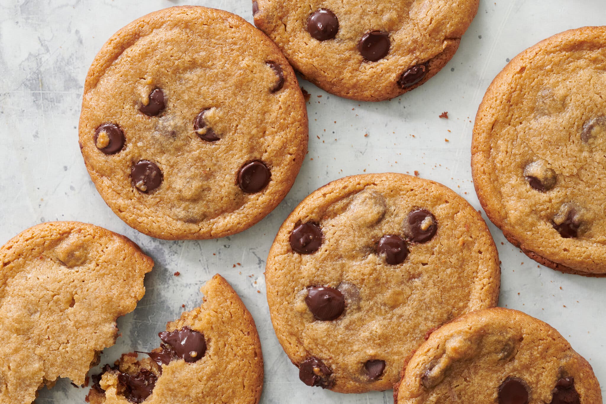 A half-dozen chocolate chip cookies are photographed from overhead.