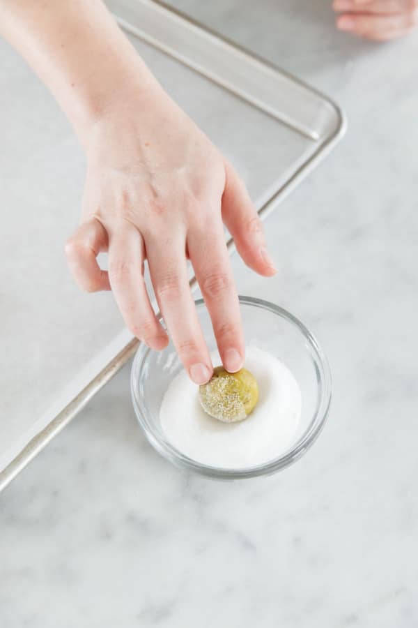 Rolling a ball of pistachio cookie dough in a small bowl with granulated sugar.