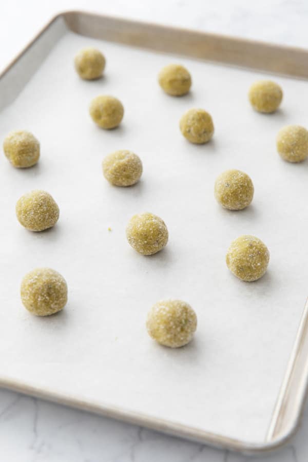 Unbaked cookie dough balls arranged on a parchment lined baking sheet.