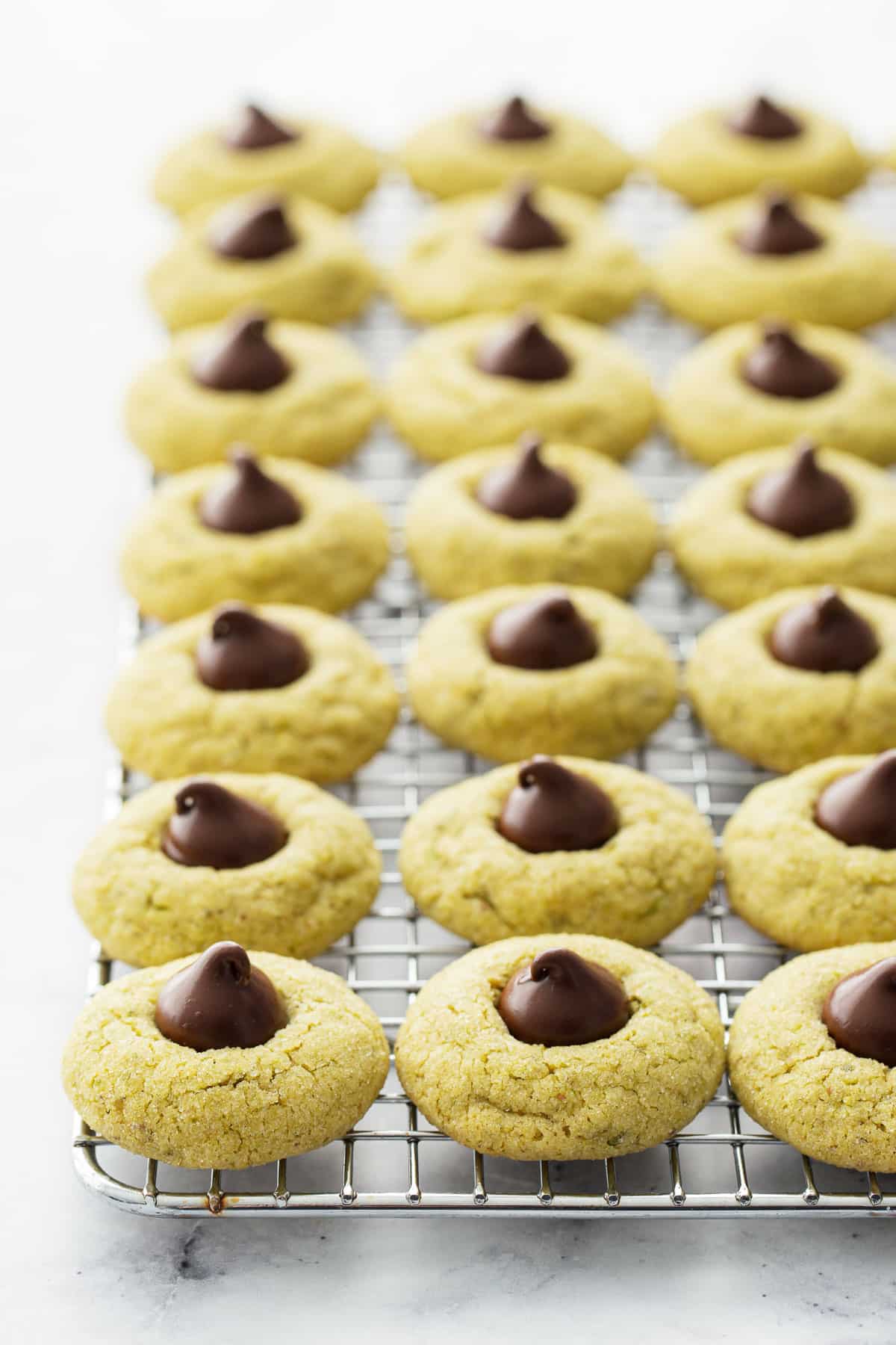 Rows of Pistachio Butter Blossom Cookies on a wire baking rack with a white marble background.