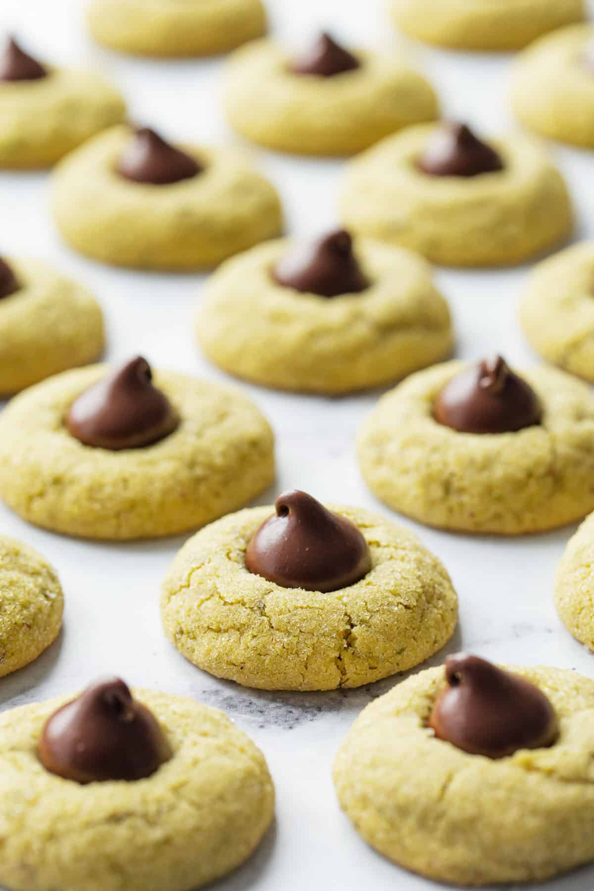 Green Pistachio Butter Blossoms with dark chocolate kisses, staggered in rows on a white marble background.