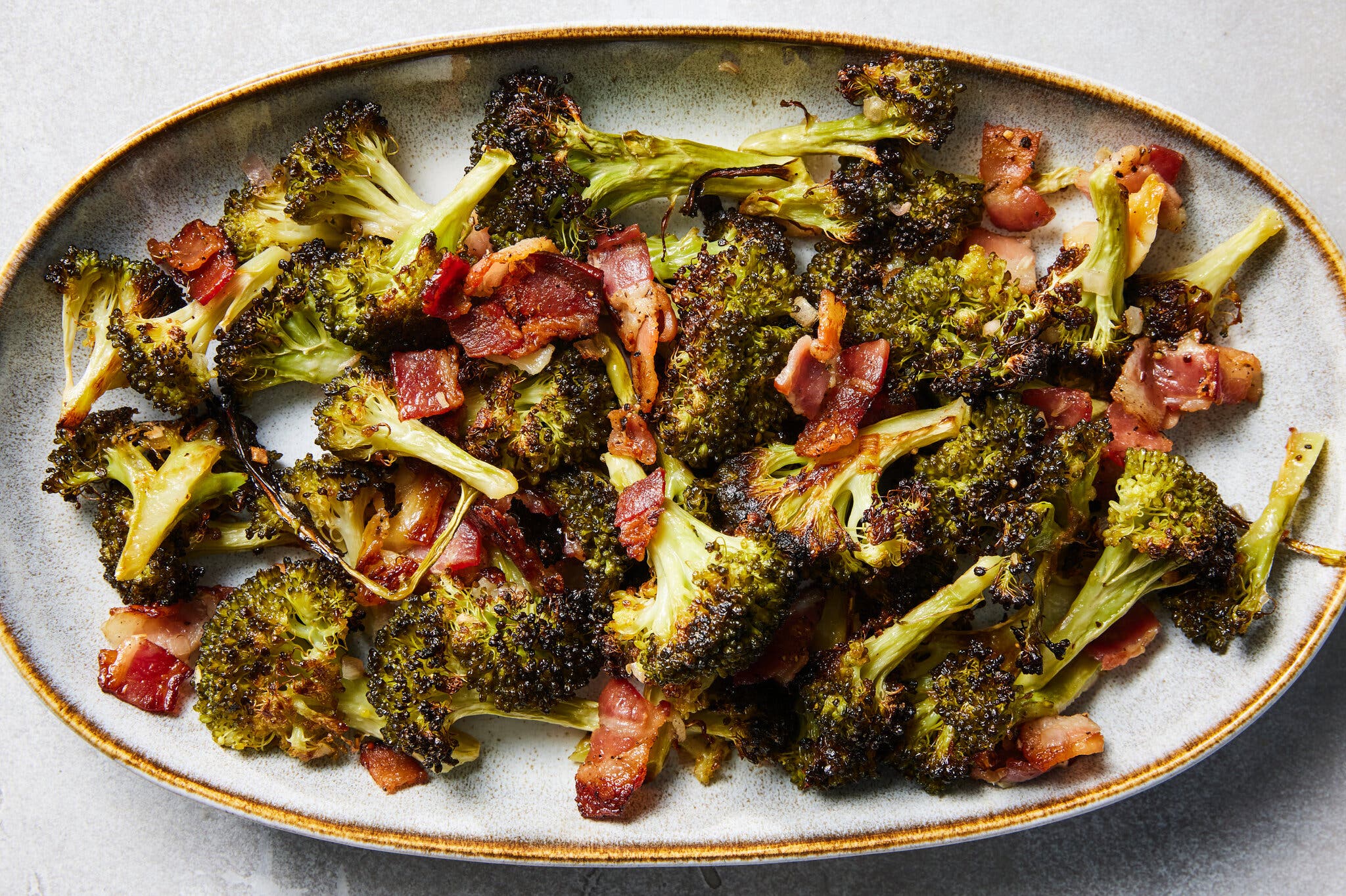 An overhead image of broccoli and bacon on a gray latter.