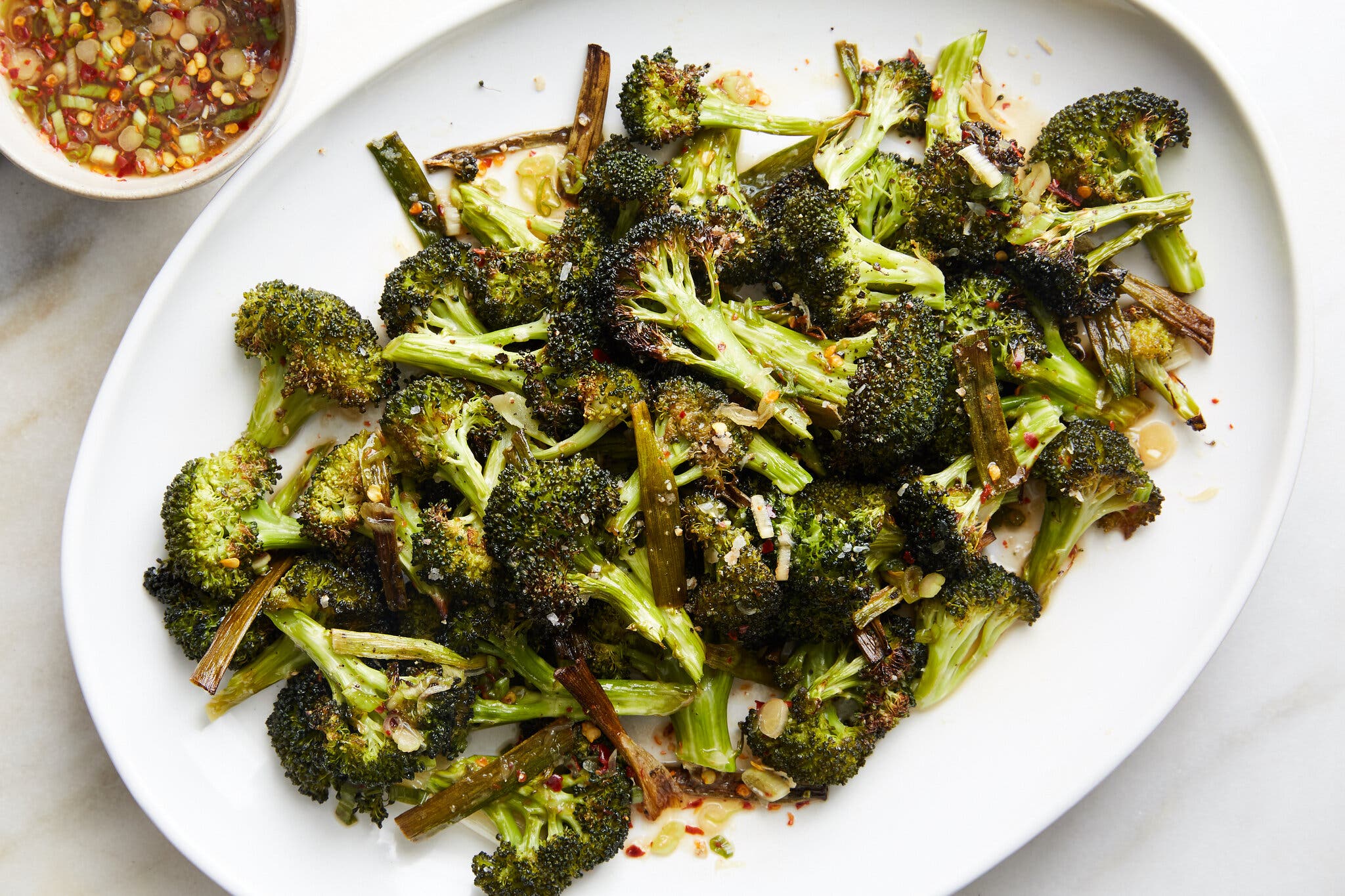 Roasted broccoli florets finished with a sauce sit on a white platter.