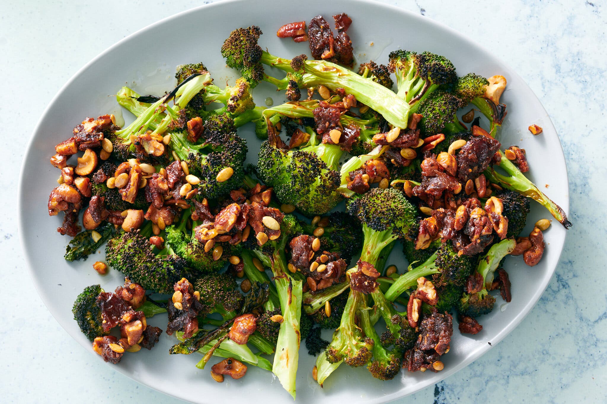 Broccoli florets, nuts and dates sit on a white platter.