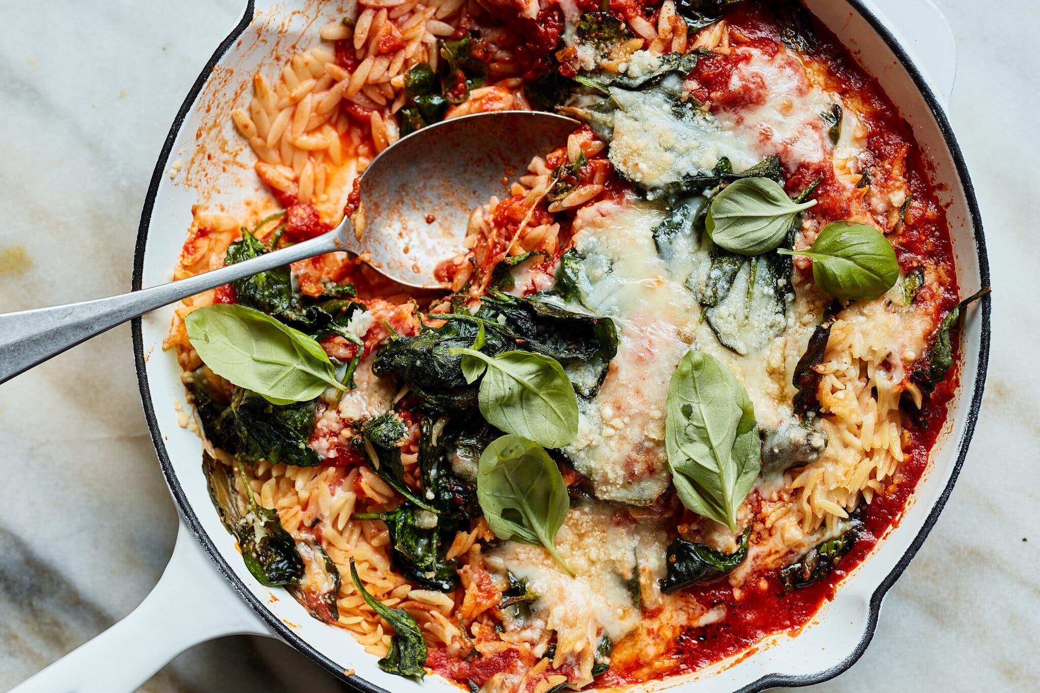 A skillet full of orzo topped with cheese and tossed with a tomato sauce.