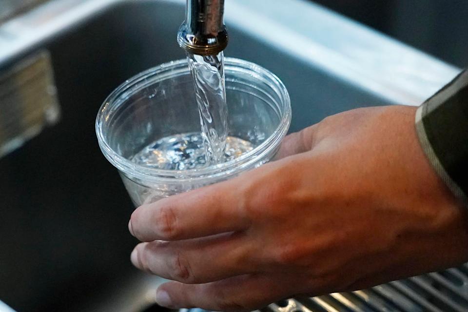 A cup collects water flowing from a faucet.