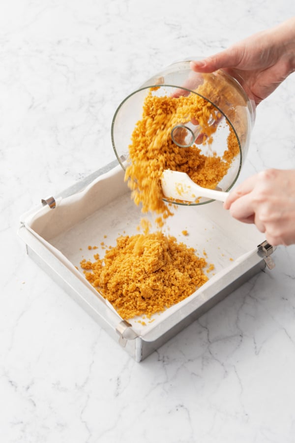 Pouring cookie crumb mixture from a food processor into a parchment-lined baking pan.