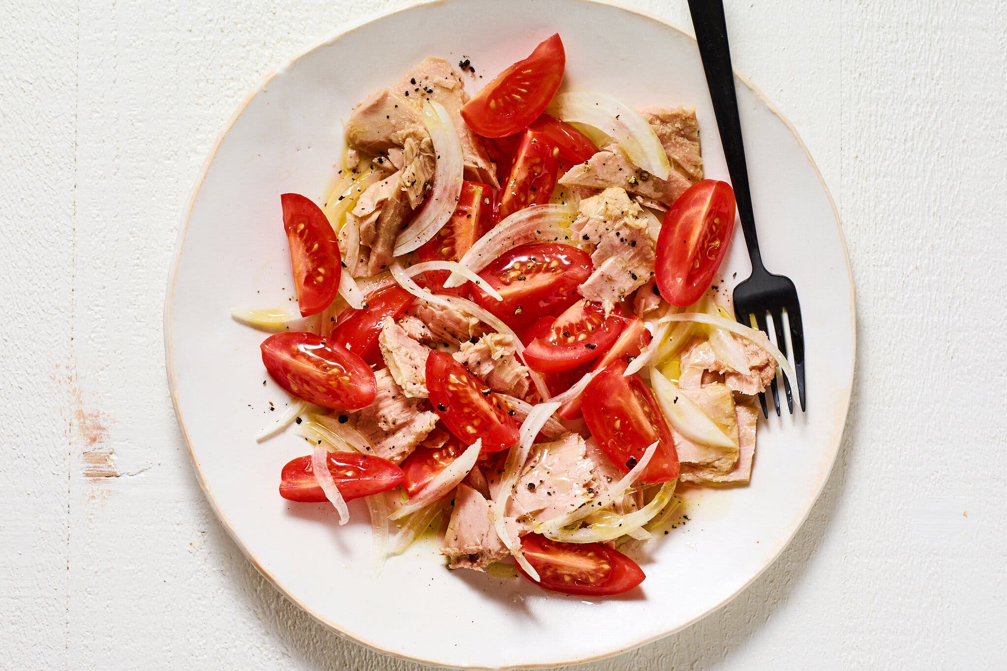 An overhead image of tuna with tomatoes and onions on a white plate.