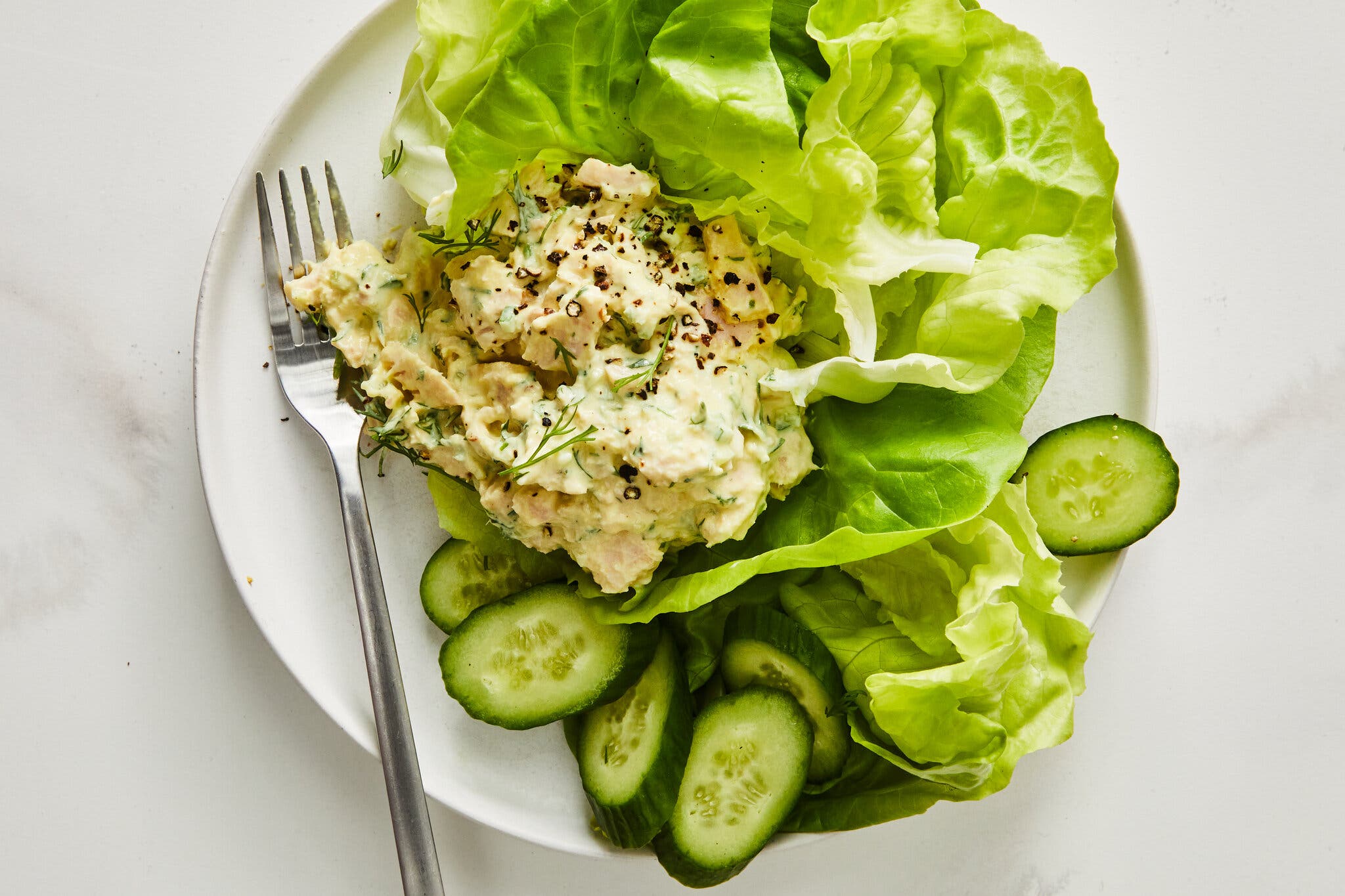 An overhead image of a tuna salad on a bed of lettuce next to sliced cucumbers.