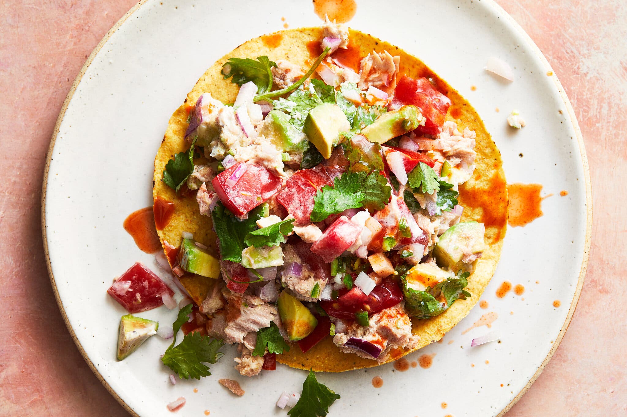 An overhead image of a tostada topped with tuna, tomatoes and avocado on a white plate.