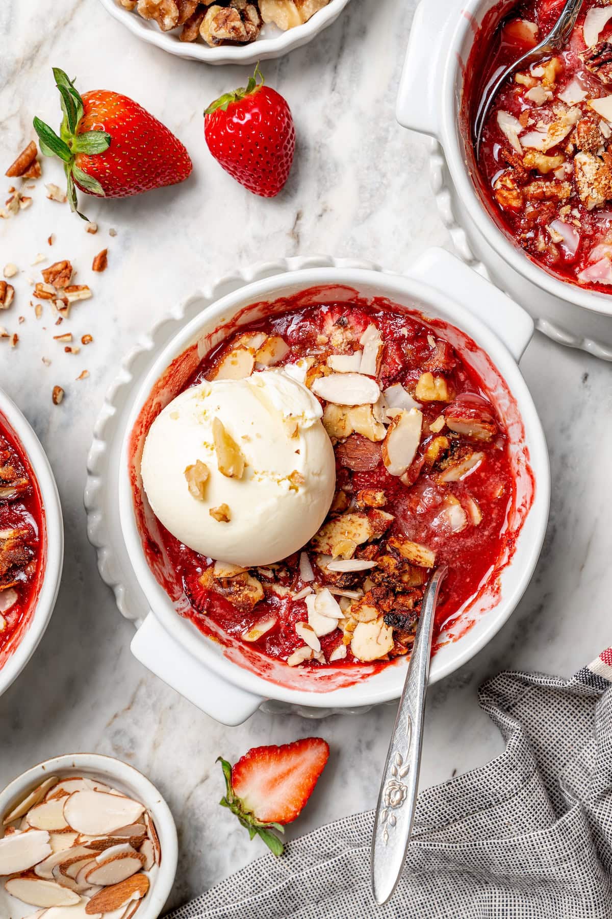 This healthy strawberry crisp recipe is perfectly portioned into individual servings, with a delicious nutty topping. So easy to make too! Overhead view of strawberry crisp in bowl with scoop of vanilla ice cream