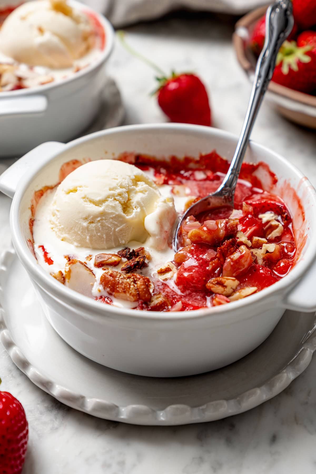 This healthy strawberry crisp recipe is perfectly portioned into individual servings, with a delicious nutty topping. So easy to make too! Spoon digging into healthy strawberry crisp topped with ice cream