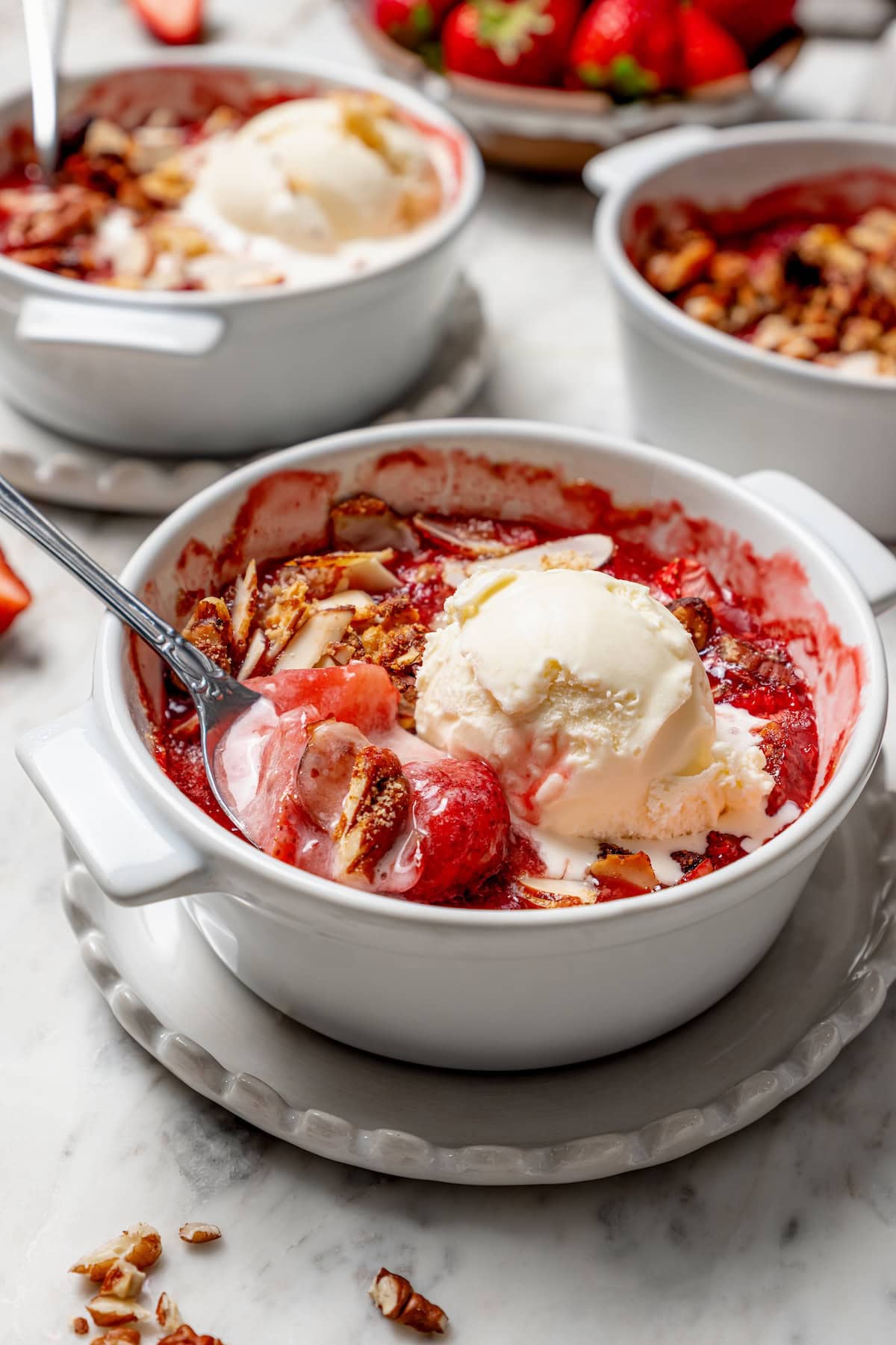 This healthy strawberry crisp recipe is perfectly portioned into individual servings, with a delicious nutty topping. So easy to make too! Strawberry crisp in bowl with scoop of ice cream and spoon