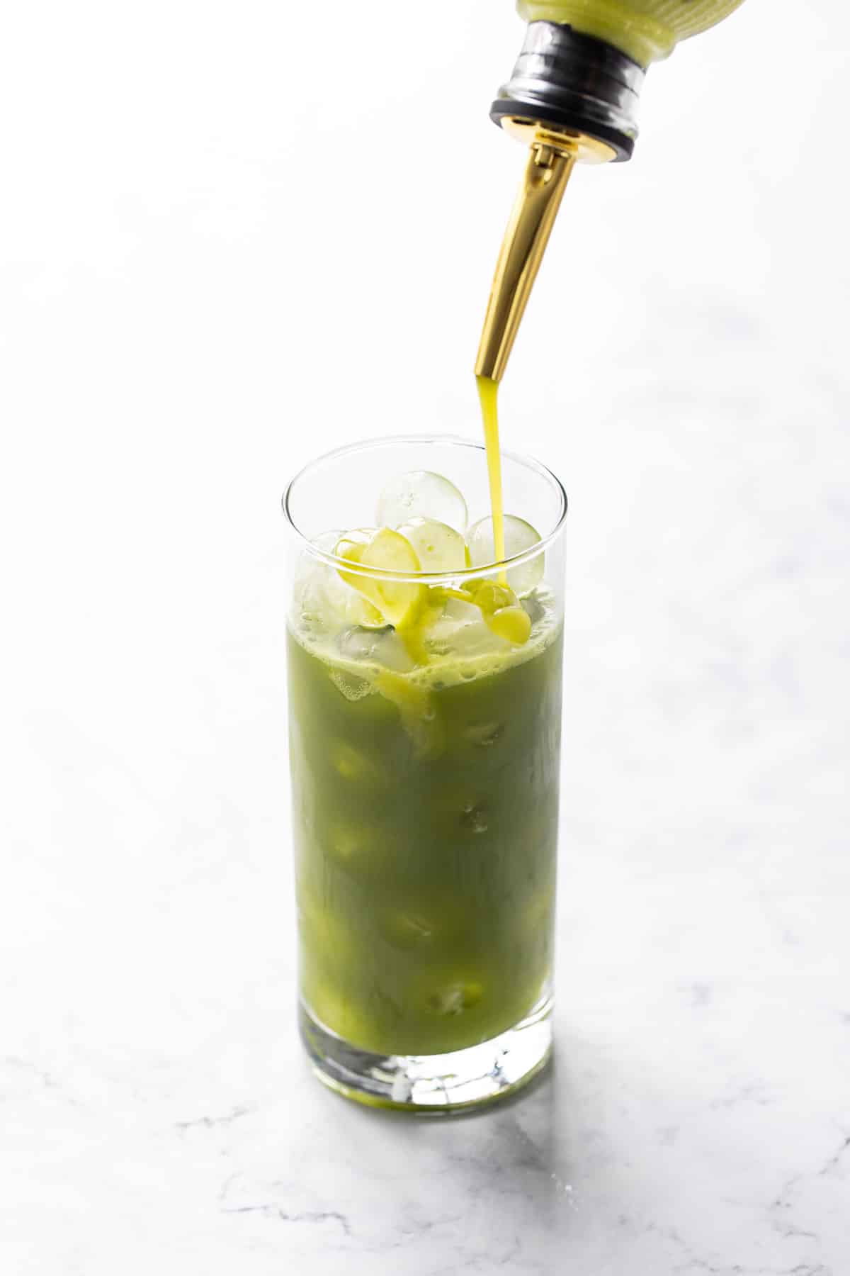 Pouring Homemade Pistachio Syrup into a glass filled with round ice cubes and bright green matcha.
