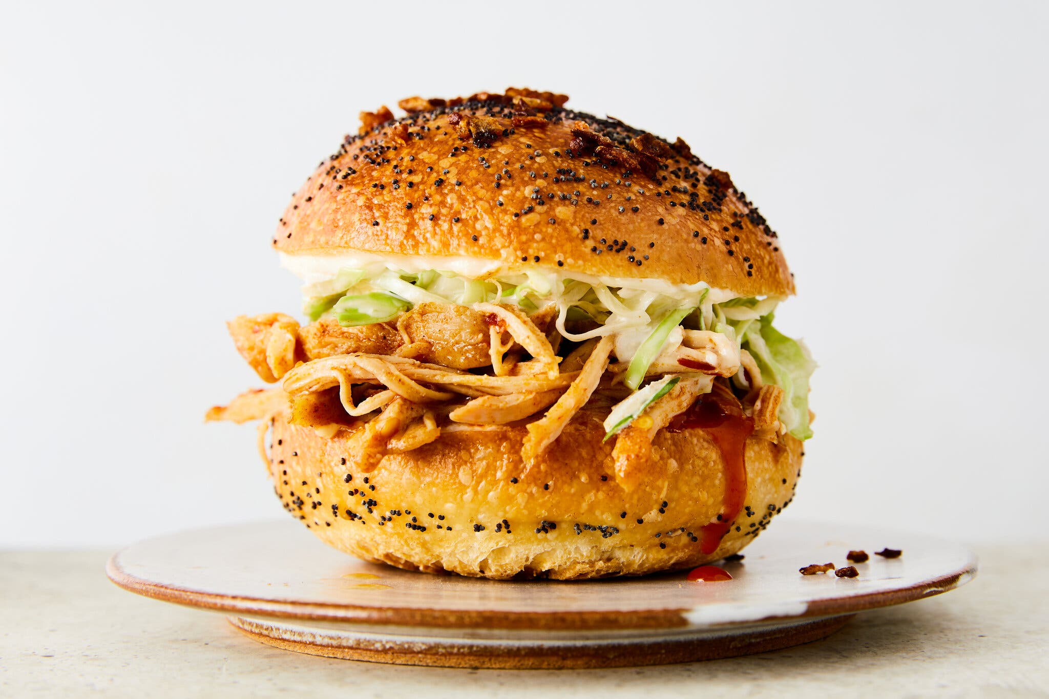 A side shot of a seeded bun filled with shredded chicken and lettuce on a brown plate.