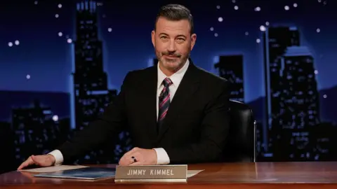Getty Images Jimmy Kimmel sits at his desk on his late night show