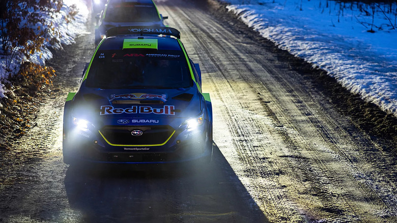 A Subaru rally car on a snow course, from the front with headlights on at night