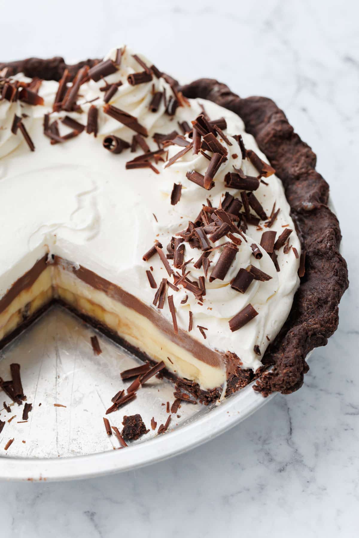 Chocolate Banana Cream Pie with Chocolate Pie Crust in a metal pie plate, with two slices removed to show the layers of chocolate and banana underneath.