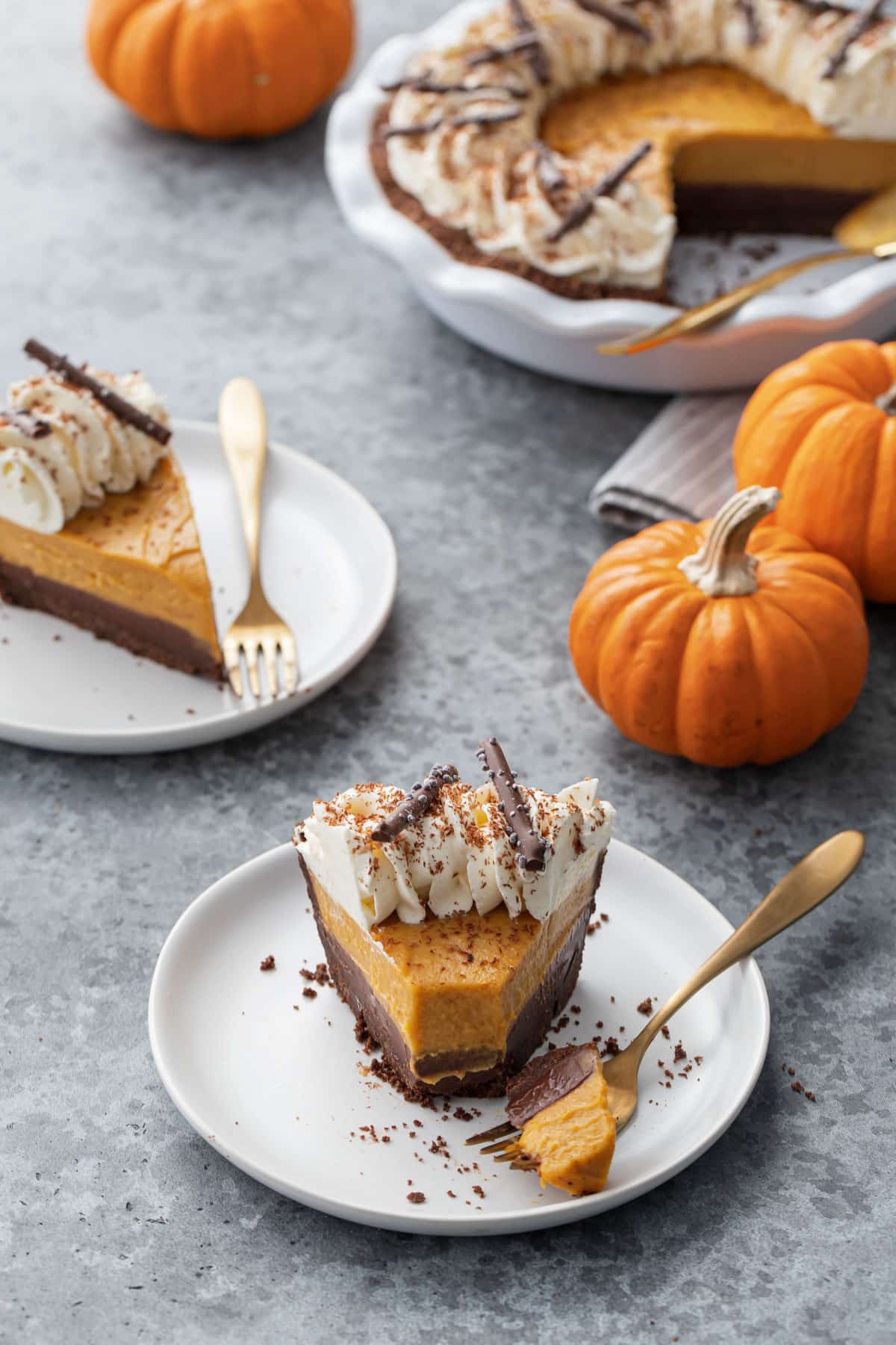 Slice ofBlack Bottom Pumpkin Cream Pie on a plate with a bite sitting on a gold fork, with mini pumpkins in the background.