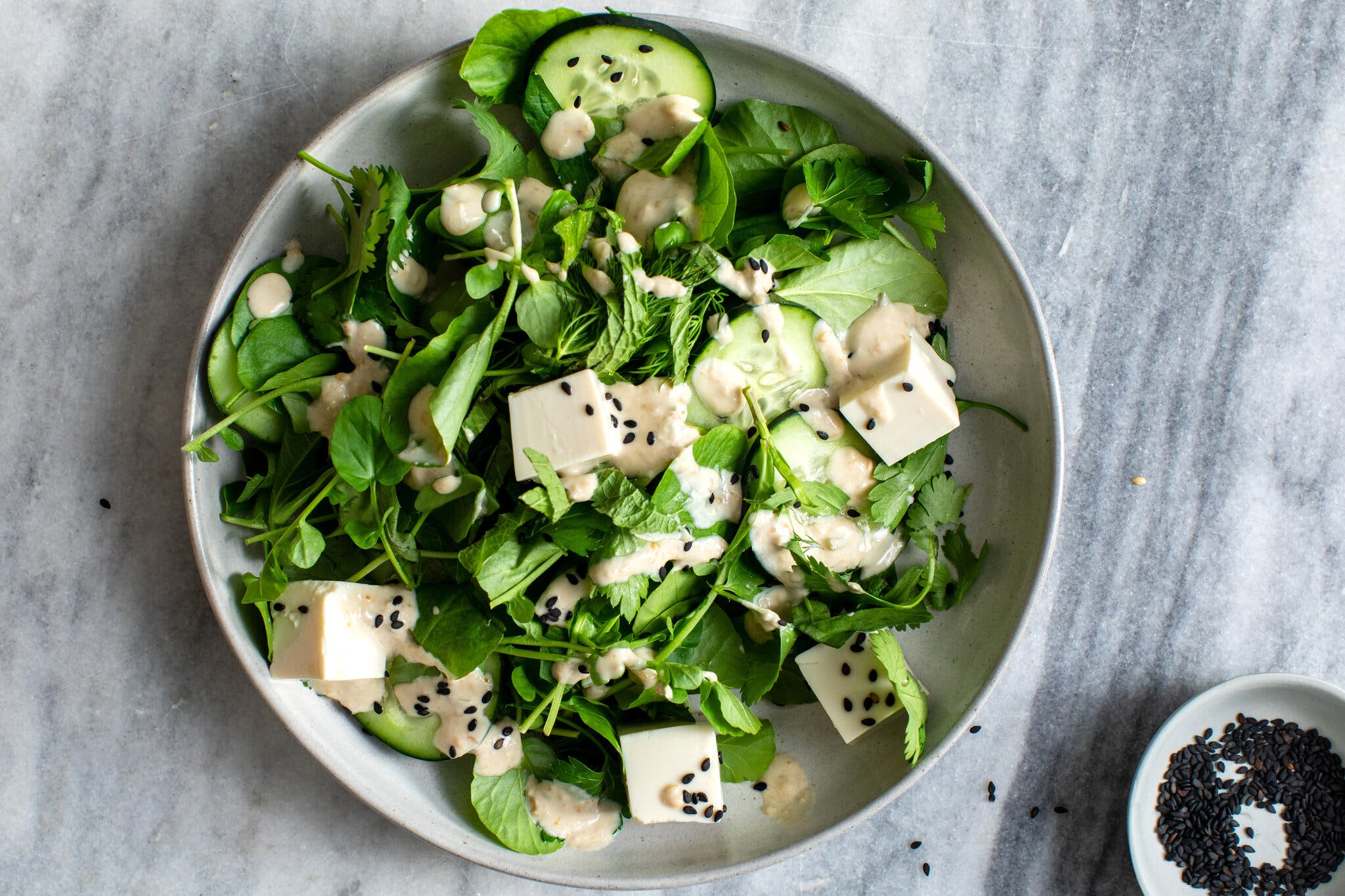 An overhead image of a salad topped with a light sauce, sesame seeds and cubes of tofu.