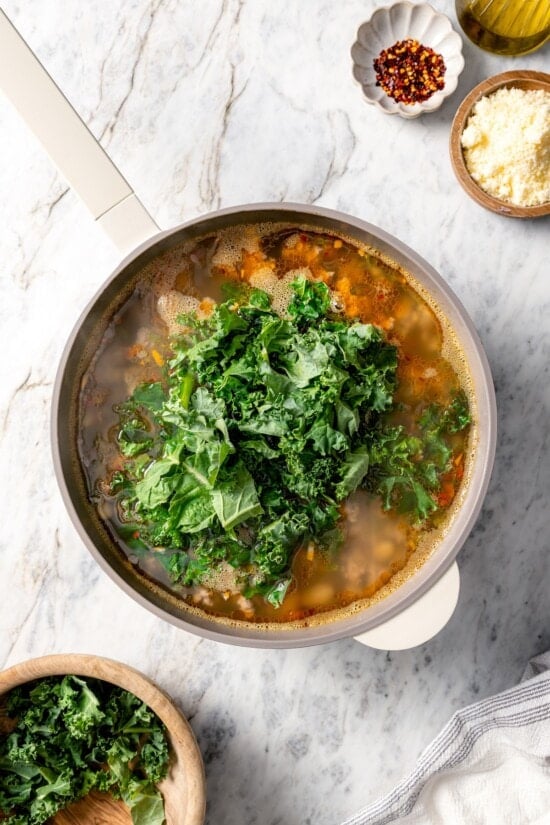 This hearty white bean soup with turkey sausage and kale is packed with protein and fiber, full of cozy flavor, and perfect for chilly days! Kale added to pot of white bean soup.