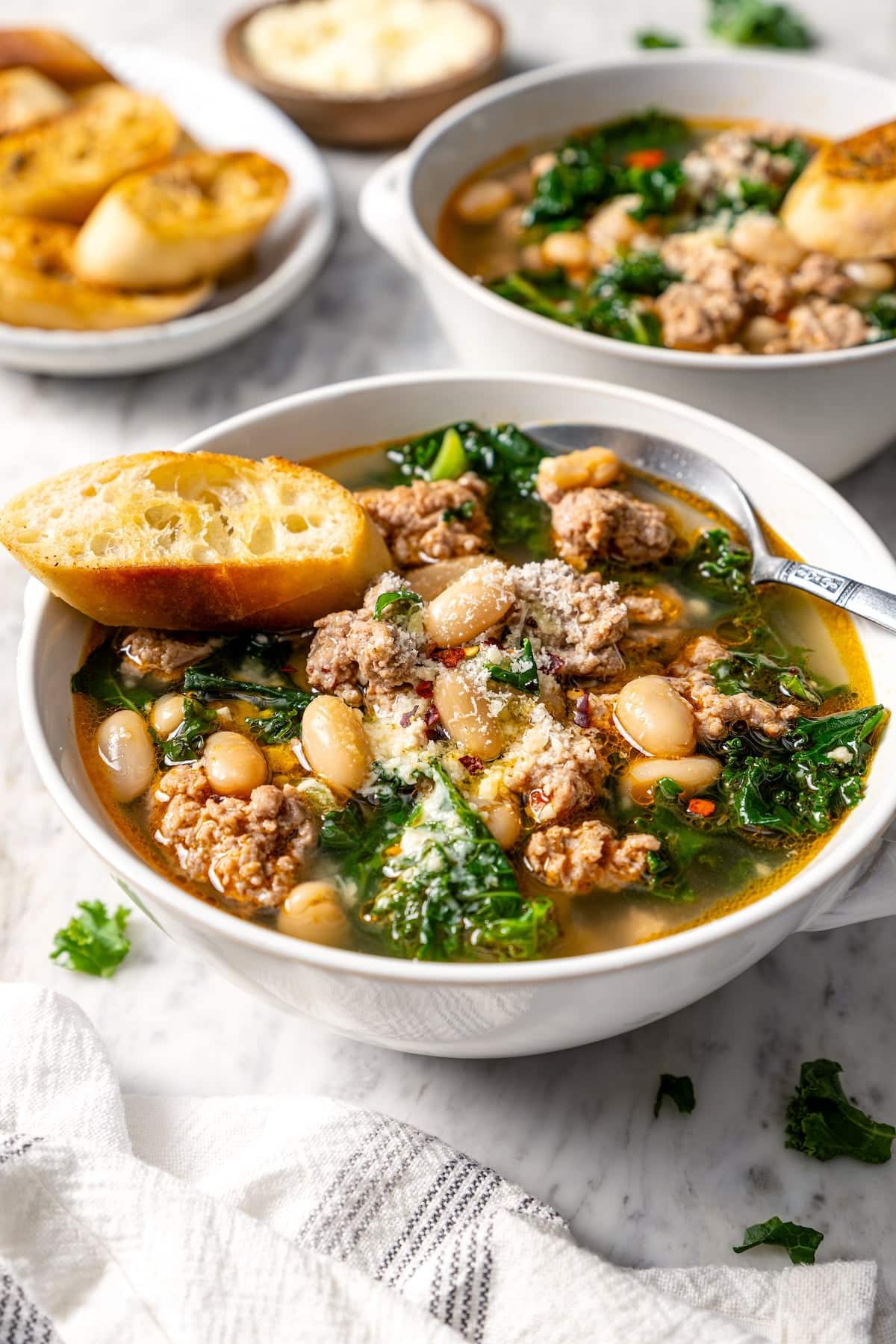 This hearty white bean soup with turkey sausage and kale is packed with protein and fiber, full of cozy flavor, and perfect for chilly days! Spoon and toast in bowl of white bean soup with sausage and kale.
